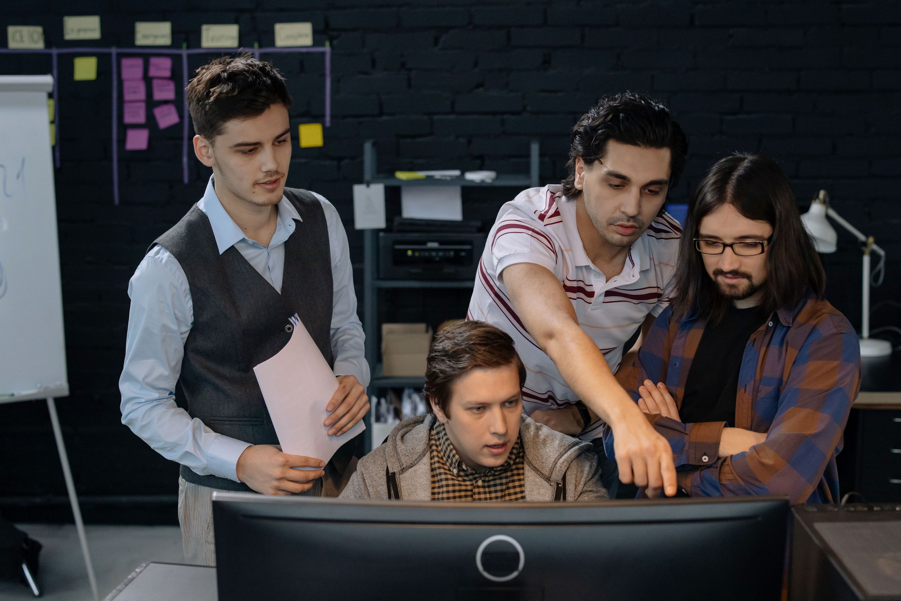 Four colleagues discussing a project around a computer in an office, one pointing at the screen